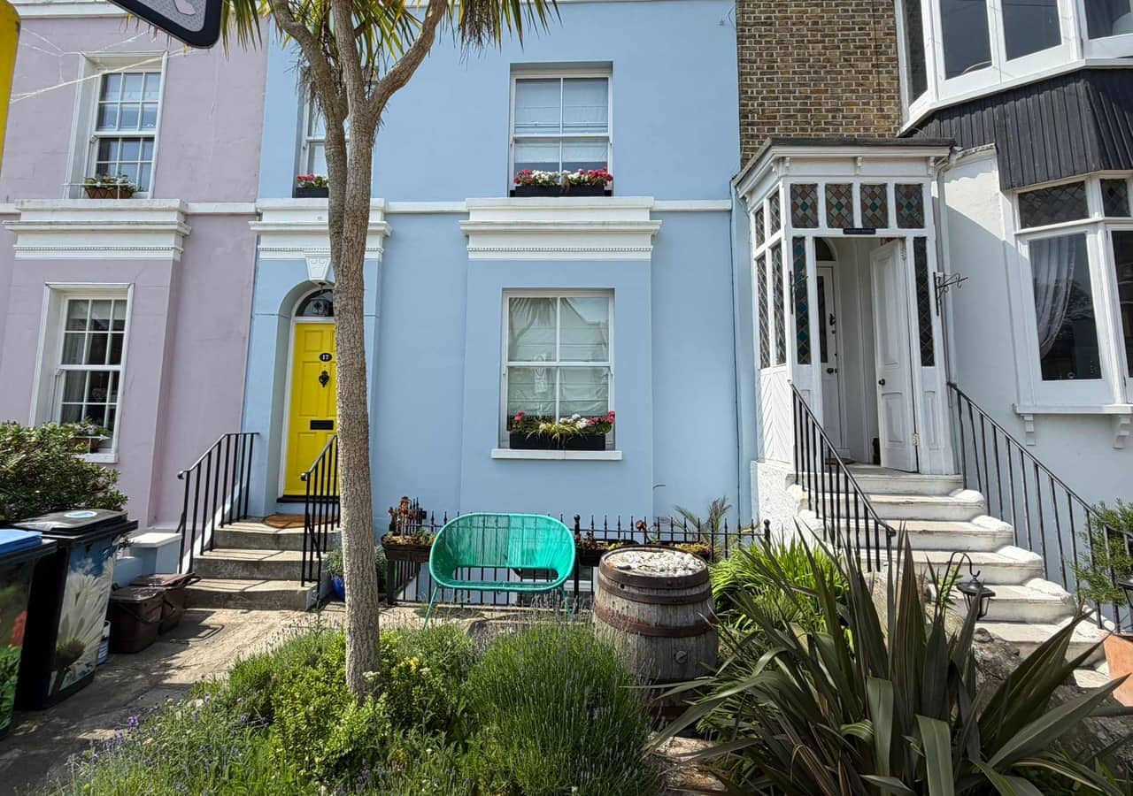 A Georgian terrace painted powder blue with a yellow front door, white window surrounds and palm trees in the front garden